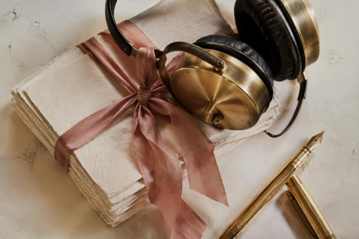 Audífonos dorados sobre tarjetas de canciones atadas con listón rosa